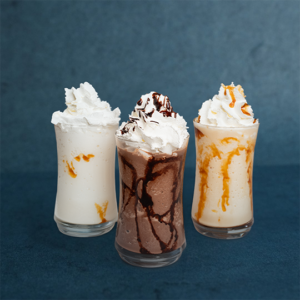 Three classic milkshakes in glass cups topped with whipped cream, featuring caramel, vanilla, and chocolate flavors.