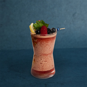 Exotic fruit drink in a tall glass, garnished with mixed berries, mint, and lemon, available in forest agave and passion flavors.