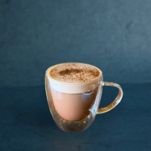 Hot chocolate served in a clear double-wall glass, topped with creamy foam and a dusting of cocoa.