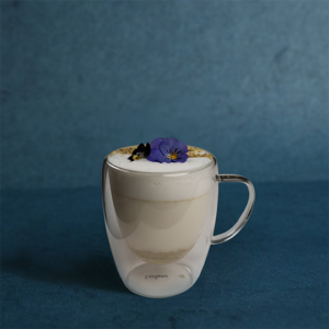 Warm pistachio beverage in a clear glass mug, finished with creamy foam and delicate floral garnish.