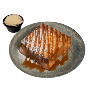 Pain perdu served on a plate, dusted with powdered sugar and drizzled with caramel sauce, with a scoop of ice cream on the side.