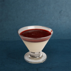 Panna cotta dessert served in a glass, topped with a smooth berry sauce.
