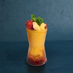 Tropical mixed fruit drink served in a tall glass, garnished with fresh fruit slices and mint leaves.