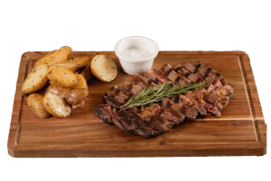 Sliced grilled ribeye steak topped with fresh rosemary, served on a wooden board with golden roasted potatoes and a ramekin of Maldon sea salt.